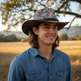 Man wearing a Rustler Leather Hatand blue shirt in a field with trees in the background