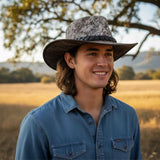 Man wearing a Rustler Leather Hatand blue shirt in a field with trees in the background