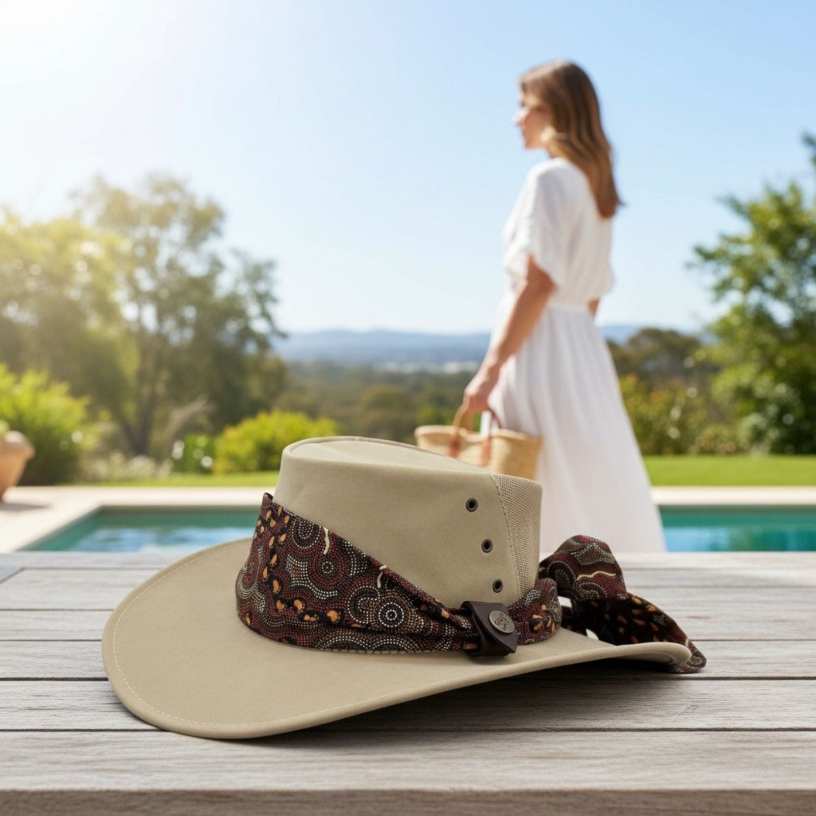 Sand Kangaroo Ladies Breeze Hat with brown band on a wooden surface with a blurred background of a pool and greenery.