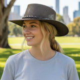 Woman wearing a wide-brimmed hat in a park with city skyline in the background
