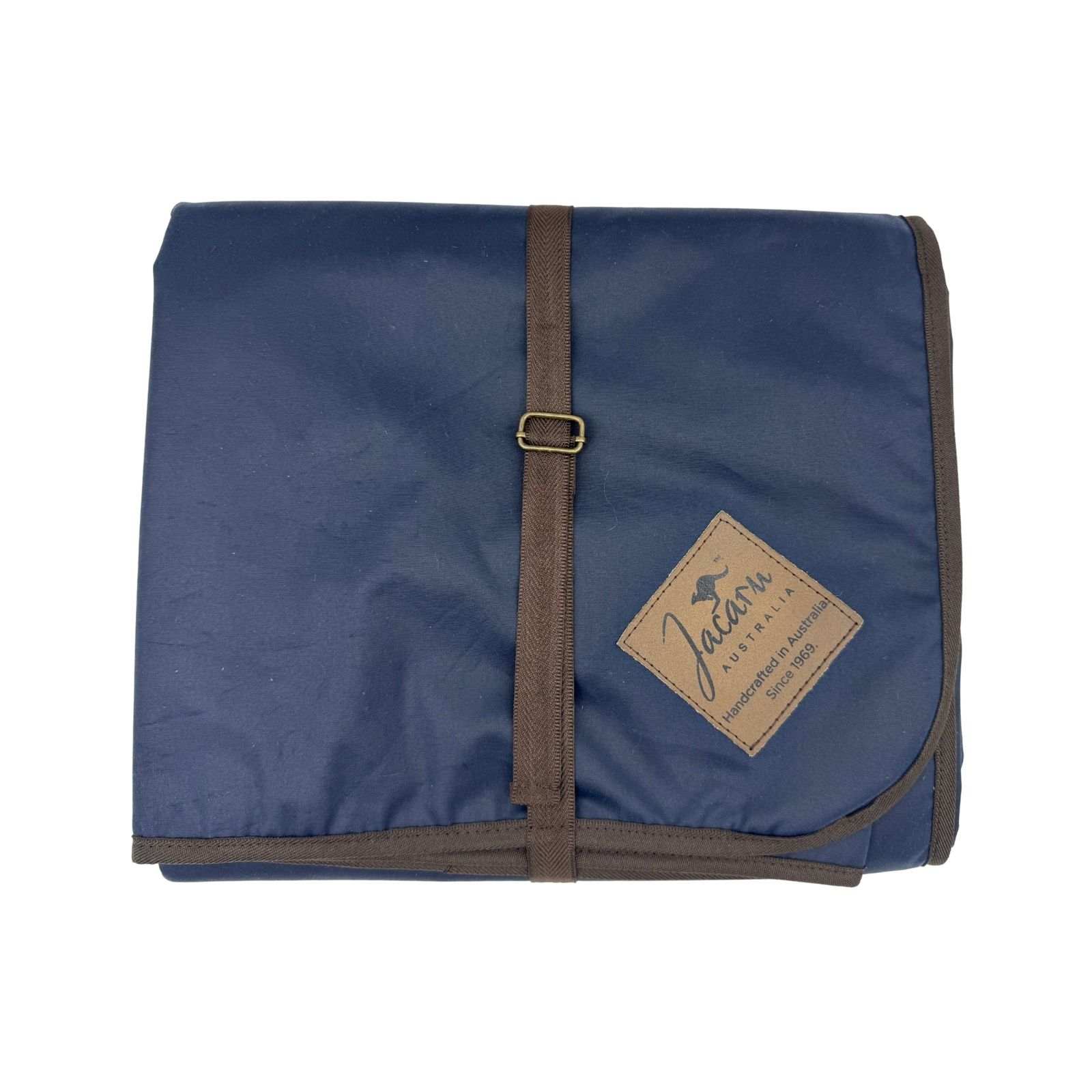 Jacaru navy picnic blanket folded with brown trim and logo patch showing handcrafted branding.
