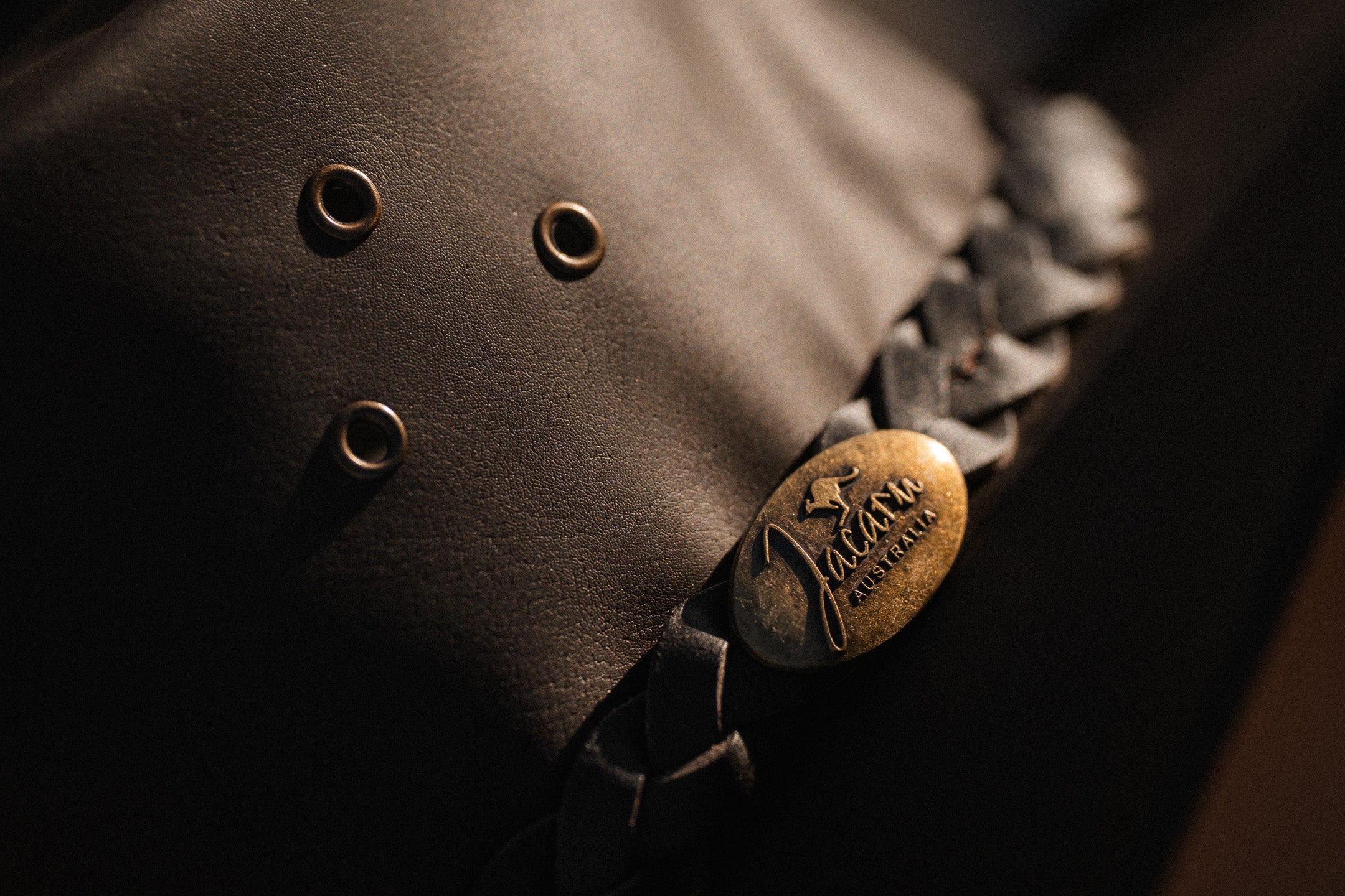 Close-up of a brown leather product with decorative elements and a brand logo jacaru