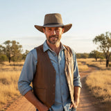 Smiling man in a Jacaru 1004M Mesh Rustic Explorer Hat - Special Edition Stonewash Brown and leather vest outdoors.