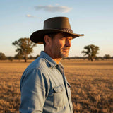 Man wearing a cowboy hat and denim jacket standing in a field with trees in the background.