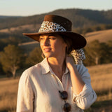 Woman wearing a Jacaru 1020 Jillaroo Hatwith a leopard print band in a scenic outdoor setting.