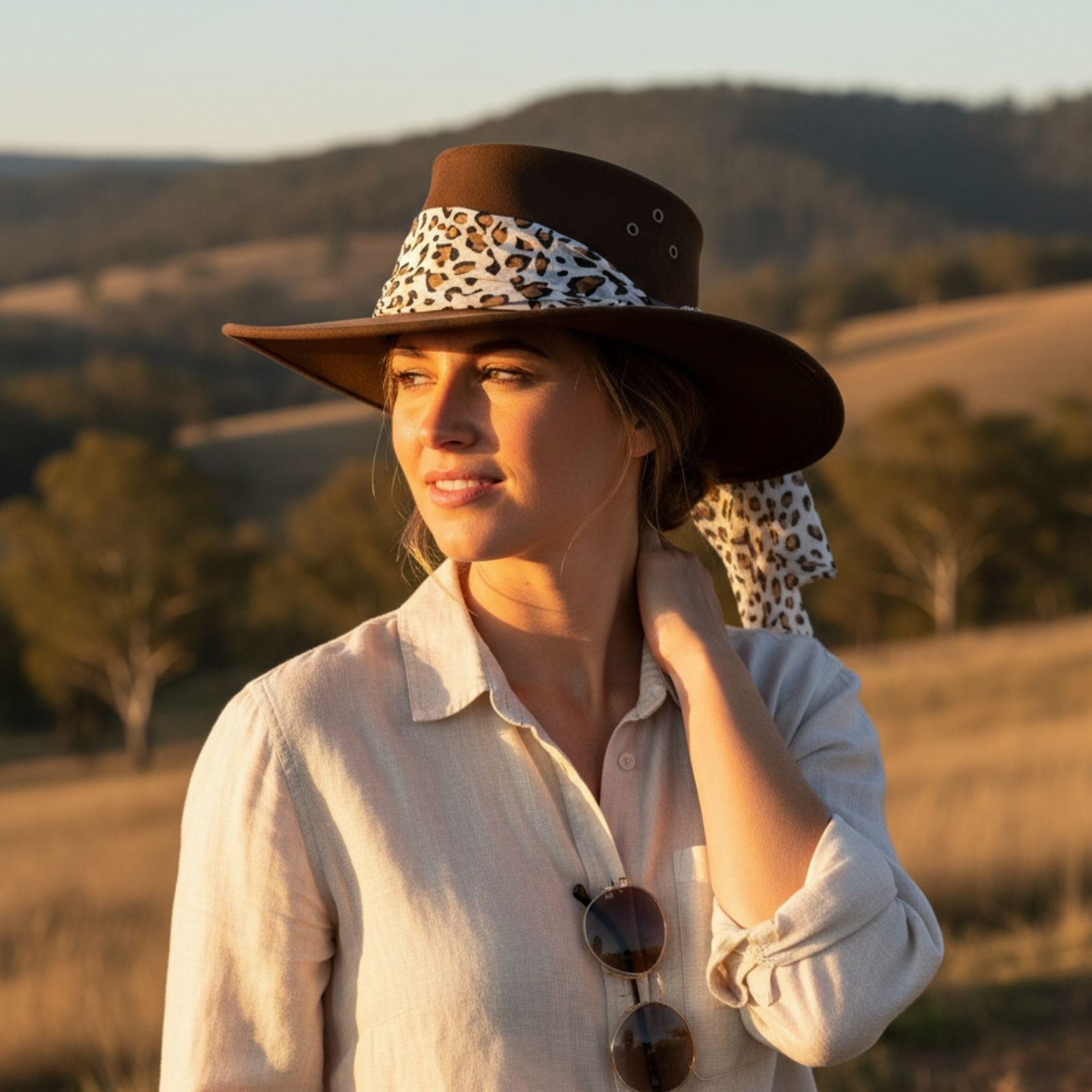 Woman wearing a Jacaru 1020 Jillaroo Hatwith a leopard print band in a scenic outdoor setting.