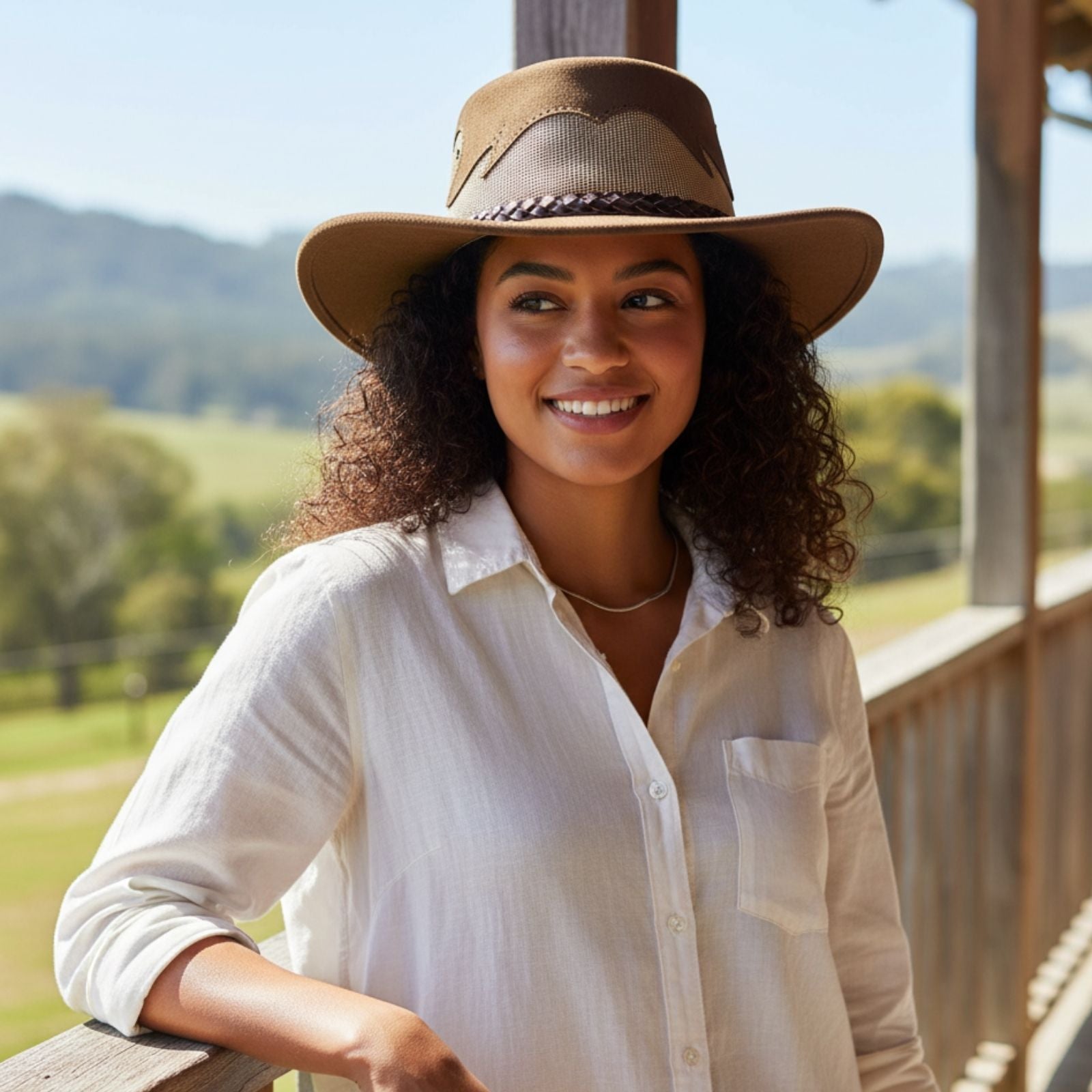 Woman wearing a Mushroom Jacaru 1021 Blaze Hat and white shirt standing on a wooden deck with a scenic background