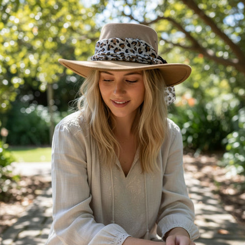 Woman wearing a wide-brimmed hat with a leopard print band outdoors.