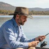 Man in a Jacaru 1026B Knockabout Breeze Hat fishing by a lake with mountains in the background