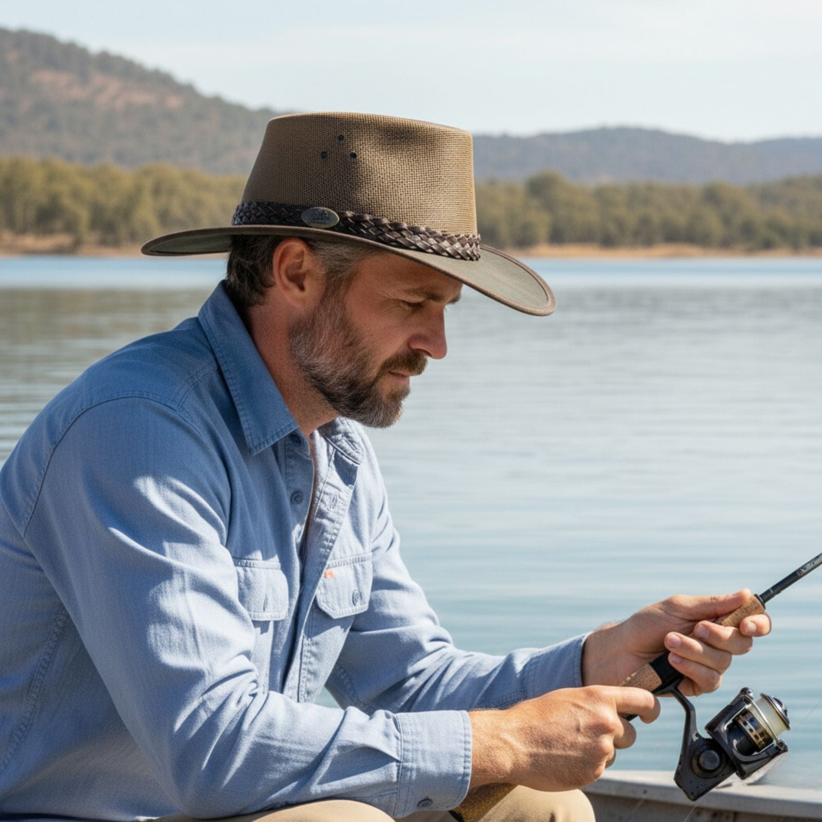 Man in a Jacaru 1026B Knockabout Breeze Hat fishing by a lake with mountains in the background