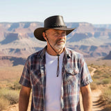 Man wearing a cowboy hat and plaid shirt standing in front of a desert landscape