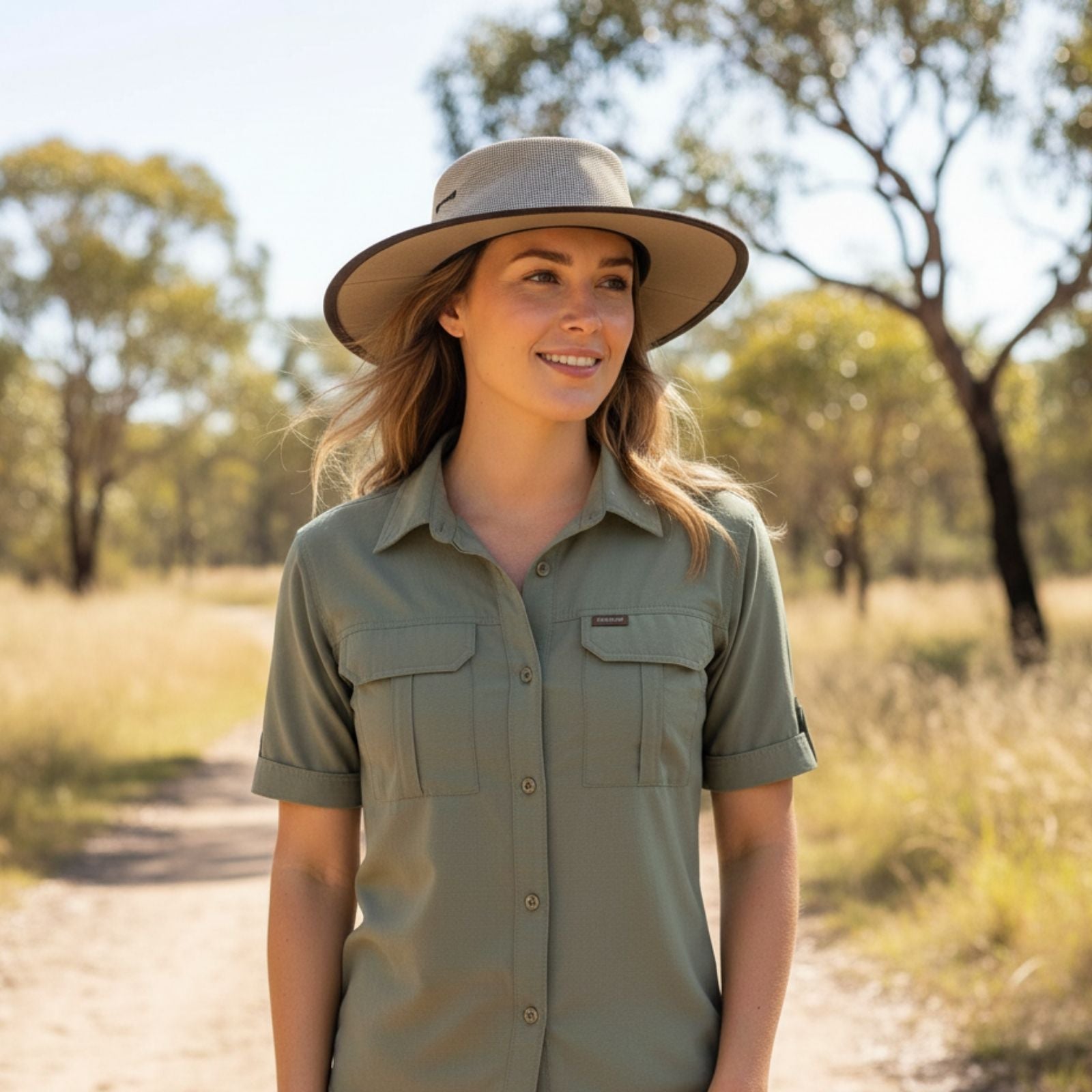 Woman wearing a green shirt and beige Jacaru 104 Bushbreeze Camper Hat in a natural setting with trees and grass.