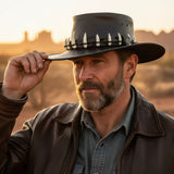 Man wearing a Lightning Jack 11 Croc Teeth Hat with white designs, holding it with a sunset in the background