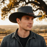 Man wearing a black Jacaru 1134 Wild Roo Croc Digger Hat and denim jacket in a rural setting with trees and a fence.