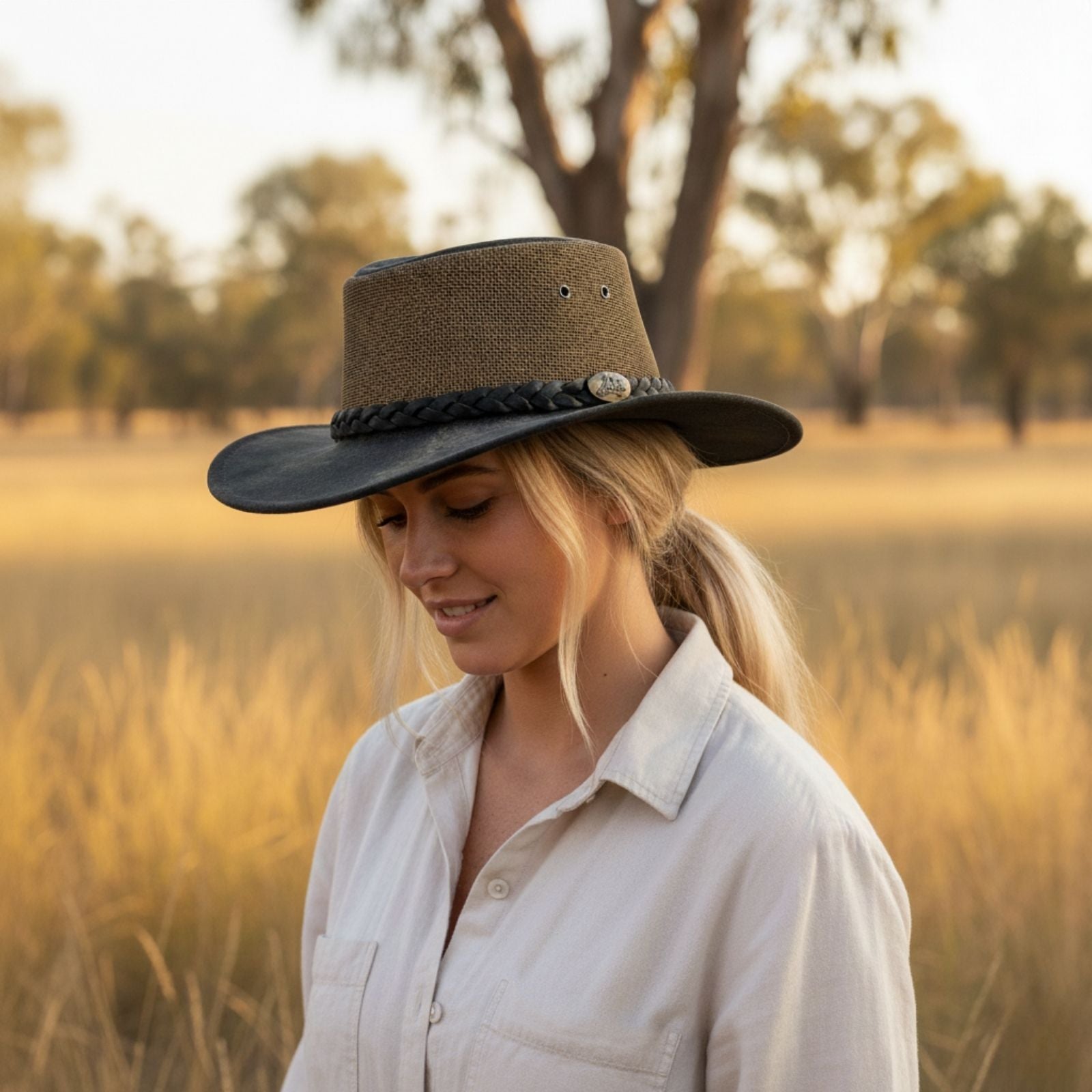 Woman wearing a brown hat in a field with trees in the background