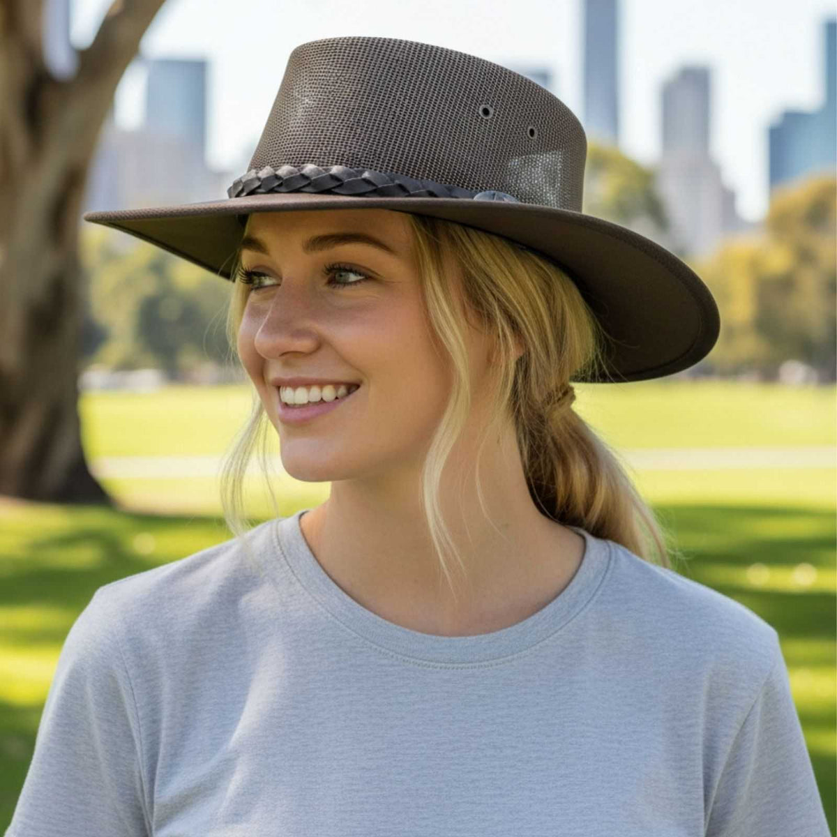 Woman wearing a wide-brimmed hat in a park with city skyline in the background