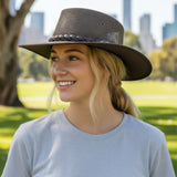 Woman wearing a wide-brimmed hat in a park with city skyline in the background