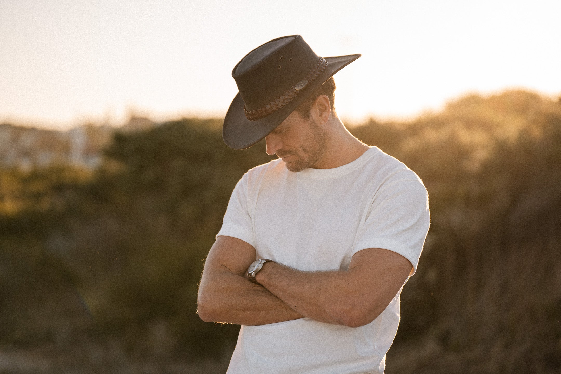 Man wearing a black hat and white shirt standing in a field with a warm glow