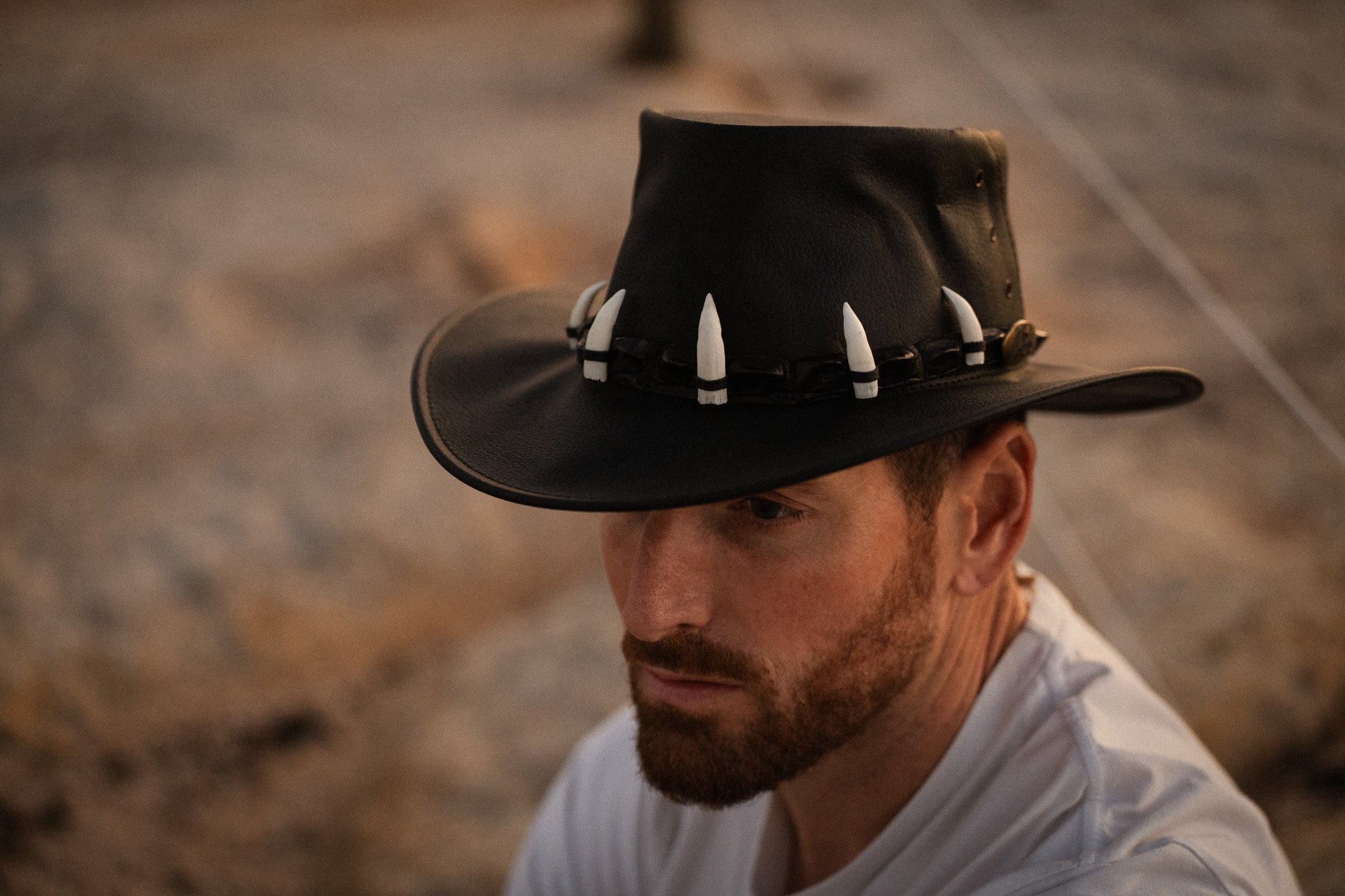 Man wearing a black cowboy hat with white bandoliers against a blurred natural background