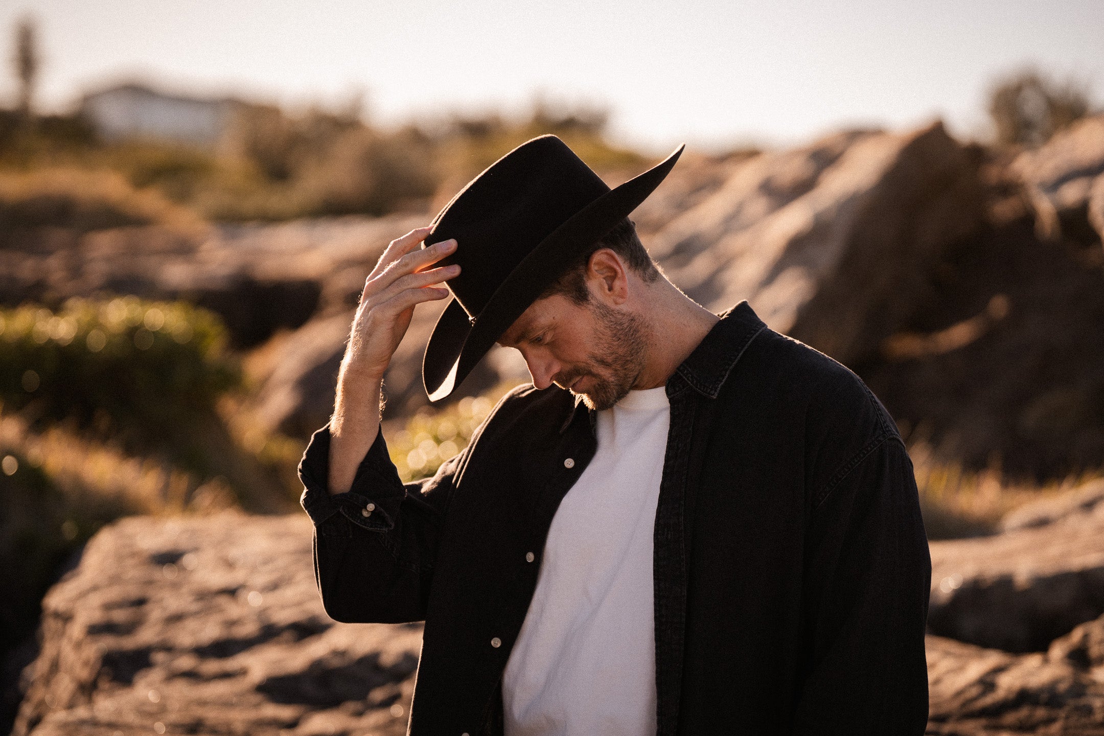 Man wearing a black cowboy hat and coat in a desert setting